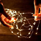 Hands holding glowing Christmas string lights in dark setting.