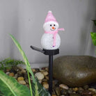 Solar-powered snowman light with pink hat and scarf in garden setting.