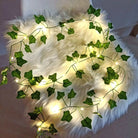 Artificial green leaf LED string lights on a furry surface, warm white illumination, flexible and energy-efficient design.